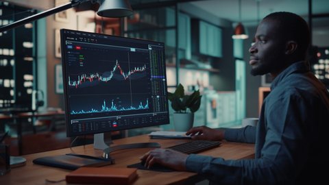 Home Office Evening: Black Financial Analyst Using Computer with Display Showing Real-Time Stocks, Exchange Market Charts. Remote Working African American Trader making e-Commerce Investment