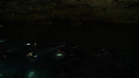 Tulum, Mexico - Nov 23 21: Group of people swimming in a Cenote with lights underwater. Turquoise pool in breathtaking underground cave. Natural pool of a sinkhole. Underground Mexican Cenotes.