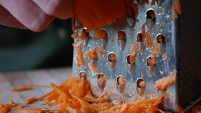 Close-up of a woman's hands grates carrots on a grater. Housewife grates carrot in kitchen.