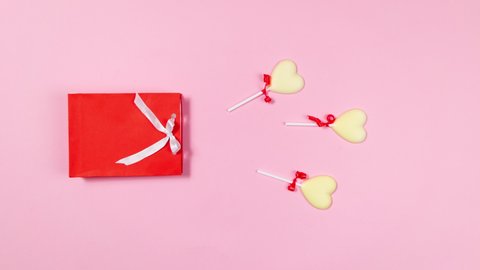 4k Heart-shaped white chocolate candies fly out of a gift red bag decorated with white ribbon. Concept of sweet gifts for holiday. Flat lay. Copy space. Stop motion animation. Light pink background.