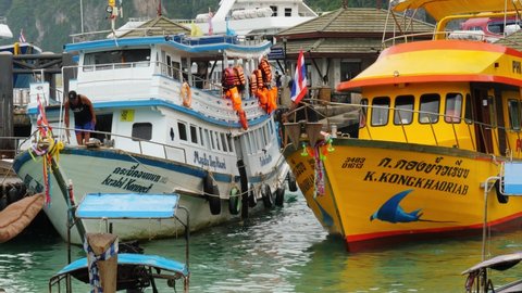 PHI PHI DON, THAILAND - APRIL 30, 2018: Time lapse shot, tourist boats mooring board to board at pier. White sightseeing boat named Krabi Konnect rock near pier, yellow scuba diving boat move aside