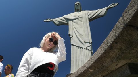 Rio de Janeiro, Brazil - Nov 23 21: Blonde girl standing under the Famous statue of Christ The Redeemer. Cristo Redentor. Jesus Statue on Corcovado mountain, 4K footage.