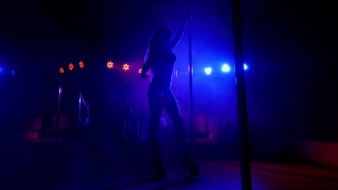Sexy woman with long flowing hair spinning around a pole in a dark room in slow motion. Pole dance.