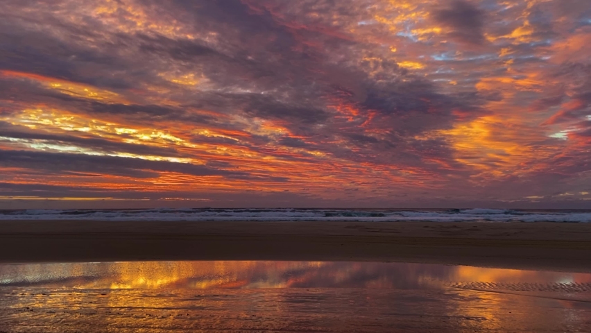 Amazing and dramatic sunrise or sunset on Australia's Fraser Island, with a stunning orange and gold palette like an oil painting, relfected in water pooled on the beach