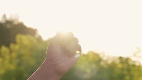 Close-up slow motion 4k video footage of one female hand showing five fingers up isolated on blurry green natural bokeh background with sparkling sun rays between fingers