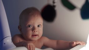Cute little toddler child standing in crib in the evening, face of happy baby boy in light of night lamp. High quality 4k footage