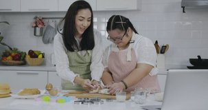 Asian girl Down Syndrome is learning to cook with her mother in kitchen at home with fun and smile. Practice making bread dough from video tutorial on laptop. Activities to improve learning skills