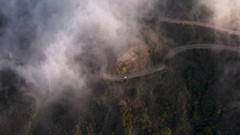 Cinematic drone footage on cloudscape flying above green landscape and empty highway road, nature 4K. Overhead aerial view on serpentine mountain road covered by thick white clouds at pink sunset