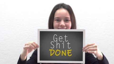 Conceptual message "Get Shit Done" on canvas frame label hold by beautiful girl smiling at camera