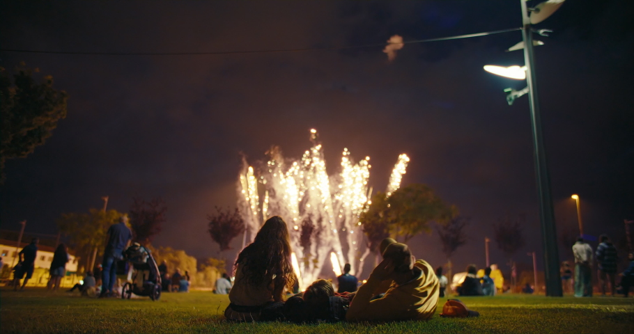 View of people gathered in park enjoy and watch incredible fireworks show, family lay on picnic blanket and look at sky on fireworks lighting up. Concept celebration or festivity on summer day | Shutterstock HD Video #1083228292