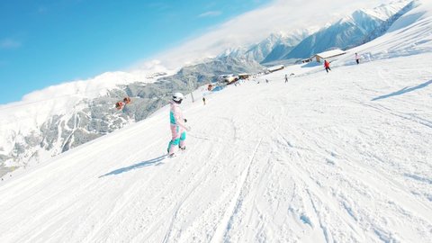 Winter holidays. Young female snowboarder rides down in the ski resort. Women snowboarder on snowboard running down the slope in Ski resort. Winter sport and recreation concept.