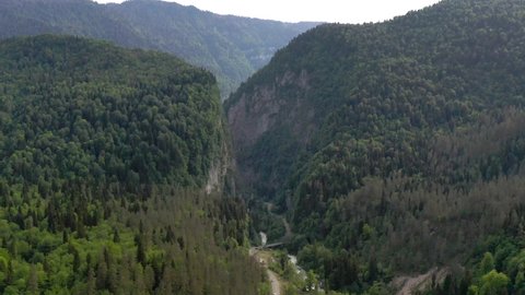Aerial view from above flying over amazing nature scenery at Abkhazia, Yupsharsky canyon. Natural environment hilly terrain covered by beautiful dense trees with small fast mountain river and bridge