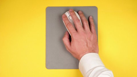 A male hand controls a white computer mouse clicks on buttons and scrolls on a gray jacket on a yellow background