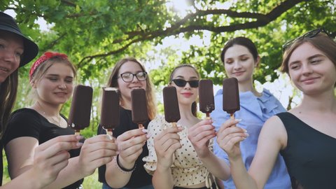 Friends hold chocolate ice cream on a stick in a row.