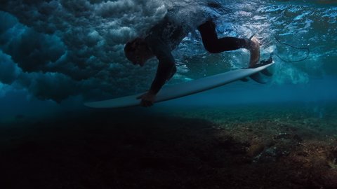 Surfer does duck dive. Male surfer dives under the wave to pass it. Underwater view of the surfer passing the wave