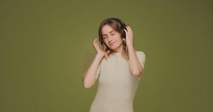 Happy young girl dj listening music with headphones, enjoying sound, dancing on green studio background