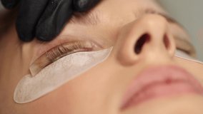 Close-up of eyelash care treatment procedures. Beautiful female, blond hair model have eyelashes lamination. Woman doing staining, curling, laminating and extension for lashes. Macro video