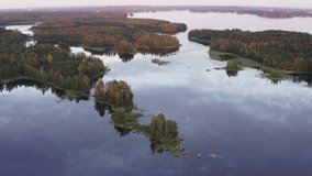 Drone video of a motorboat approaching between small islands in the distance on a calm lake scenery by golden hour after sunset.