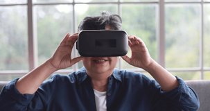 Senior old Asian woman sitting in home living room finished playing virtual reality glasses, put off with feels exciting and satisfying. Concept of retirement people learning new tech experience.
