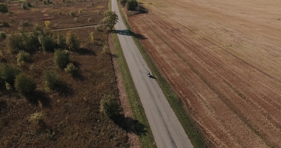 Aerial view of two people riding a motorcycle on a country road.