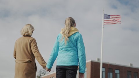 Mom and child hold hands and look at the American flag in front of the office building