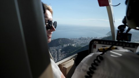 Rio de Janeiro, Brazil - Nov 23 21: Blonde young girl inside a Helicopter is enjoying a view of Christ the Redeemer statue on the top of Sugarloaf. 4K footage of Pure happiness. Cristo Redentor.