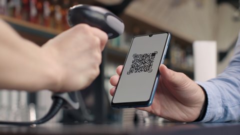 Pay by qr code on phone screen at coffee bar. Qr reader scans electronic card to transfer e-money of client wallet. Payment scanner in barista hands closeup. Male buyer in cafeteria or food market