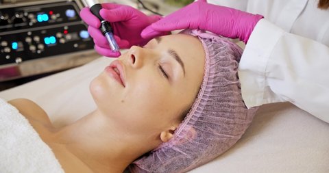 Cosmetologist making a woman a therapeutic laser processing on a face. Beautician makes skin care procedure on a  face. Woman in a spa salon on cosmetic procedures for facial care. 