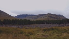 4K Tracking shot of Scottish countryside showing roadside, trees, sky, mountains and lake.