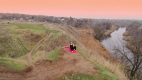 Aerial video. Young woman doing yoga in quiet scenery. Yoga girl practicing pilates on top of the hill. Yoga, sport and healthy lifestyle concept