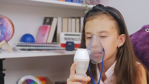 Little girl makes inhalation with medical nebulizer while sitting at the table.