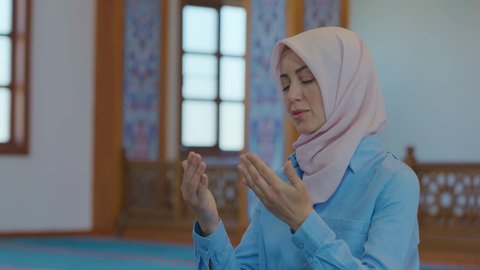 Muslim woman in hijab praying in mosque. Concept of worship during Ramadan and religious holidays. Hijab woman praying or praying while touching mihrab or head printed on mosque carpet. 