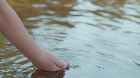 Close-up of a child's hand playing with water. A boy washing his hands on the shore of a lake.