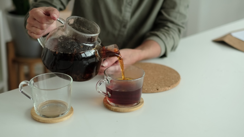 woman in a linen shirt pours tea into two transparent cups. hospitality concept, hostess treats guest to tea