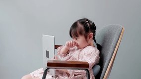 Asian child with fringe in hair sitting on chair laughing while using digital tablet.