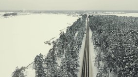 Fabulous winter landscape with a forest and a country road, aerial view. Everything is covered with white snow. Video screensaver, footage in cloudy weather for intro, background, titles. UHD 4K..