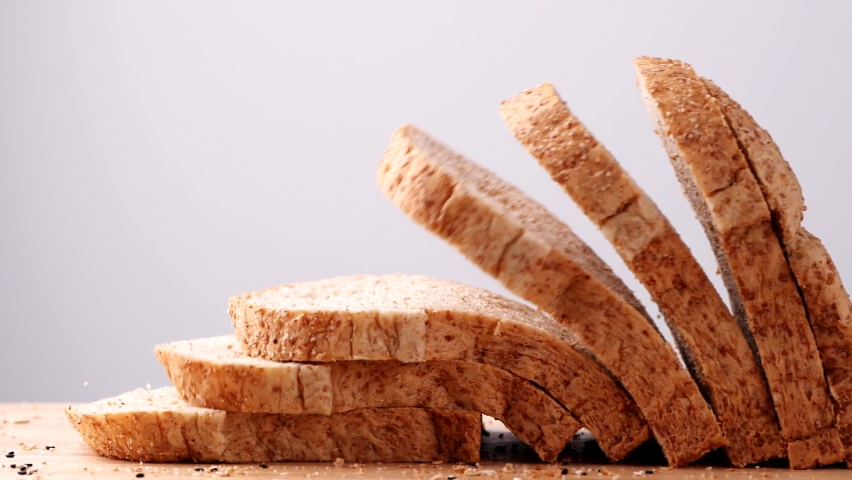 Close up whole wheat multigrain bread sliced falling on wooden table on white background, slow motion. Loaf of Bread, Slice of food, Healthy Food Concept. Royalty-Free Stock Footage #1083270916