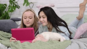 Two teen girls sit at the laptop and look at the monitor chatting with friends over video chat.