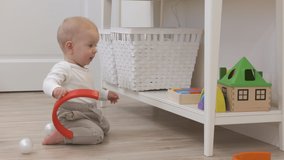 Little baby boy playing with toys on the floor at home, cute kid holding wooden rainbow stacker. High quality 4k footage