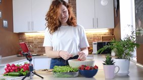 young caucasian woman at house kitchen tells recipe on camera while making salad. Online broadcast, author leads blog or course about cooking.