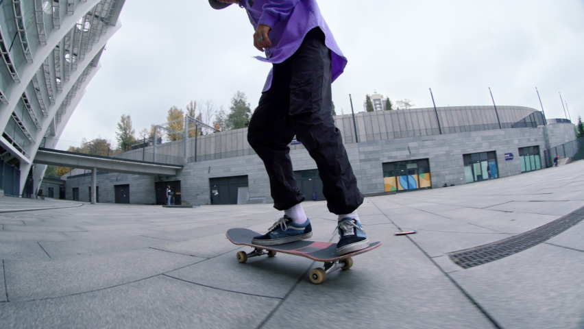 Bottom view of skater guy riding skateboard on urban background. Focused hipster making kickflip with skate outdoor in slow motion. Sporty skateboarder practicing in extreme sports outside in summer. | Shutterstock HD Video #1083276718