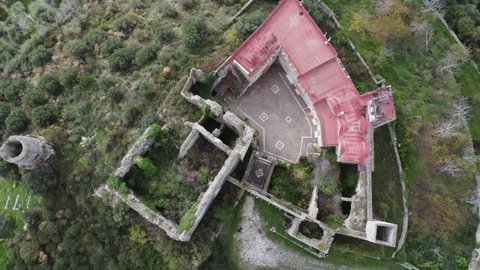 Aerial top down ascending view of Norman  Lombard ruin abandoned castle of Middle Ages  Medieval time in Nola near Naples, surrounded by olive trees on cultivation terraces moved by the wind - 4K