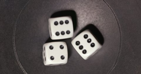 Plastic playing gambling dice rolling forever against dark background