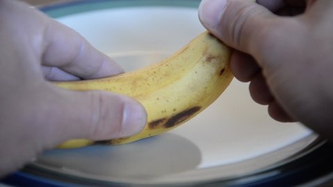 Hand peeling a banana fruit on a plate