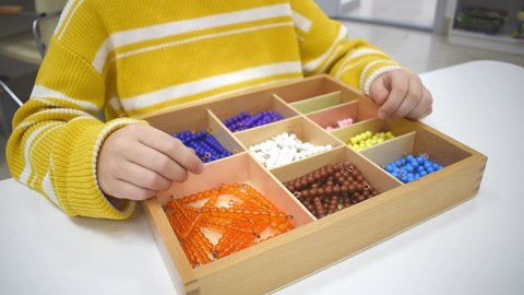 Girls hand is playing and sorting a puzzle of colored wooden geometric shapes in montessori school. Concept of using a mathematical geometry learning resources for children education.