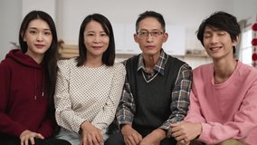 smiling asian family of four waving hand and talking to camera while filming happy chinese new year wish video with congratulation gesture at home