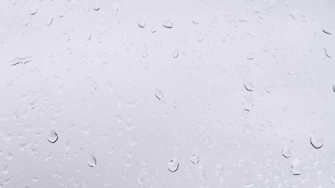 Raindrops on a transparent window run down a vertical surface. Wet window with water, natural template for splash.