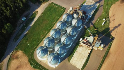 4K Aerial Elevated Top View Modern Granary, Grain-drying Complex, Commercial Grain Or Seed Silos In Sunny Spring Rural Landscape. Corn Dryer Silos, Inland Grain Terminal, Grain Elevators In A Field.