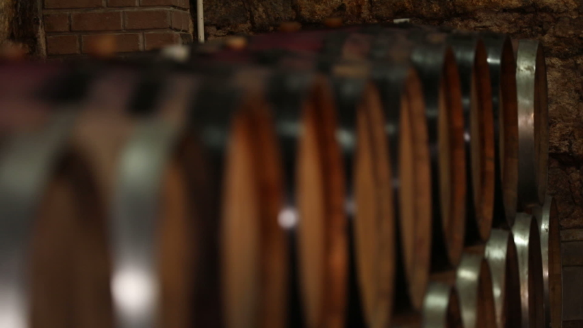A Wine Cellar. Storage Room for Wine in Bottles and Barrels. Old wine in a dark underground vault. Wooden oak whiskey, wine, cognac, brandy or beer barrels. Bottles on wooden shelves.