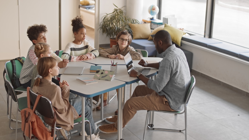 High-angle slowmo of multiethnic 5 or 6 grade students and young male African-American teacher in casualwear sitting in circle in bright classroom having funny interesting Geography lesson - Powered by Shutterstock - Get 15% off with code: PIKWIZARD15